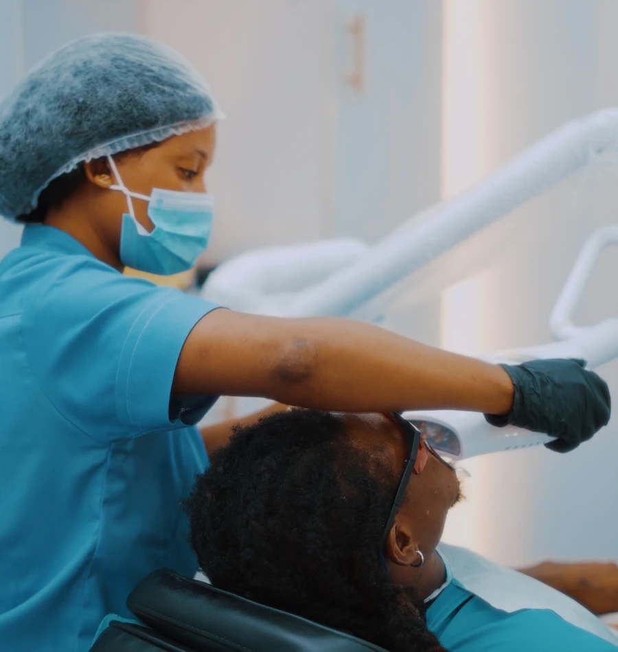 A dental assistant in teal scrubs gently adjusting the lamp over a relaxed patient