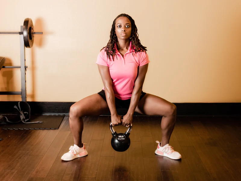 Woman doing a kettlebell sumo squat in a bright studio