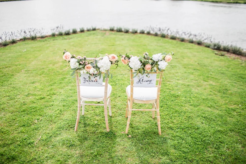 Two wooden chairs decorated with pink and white flowers on a green lawn