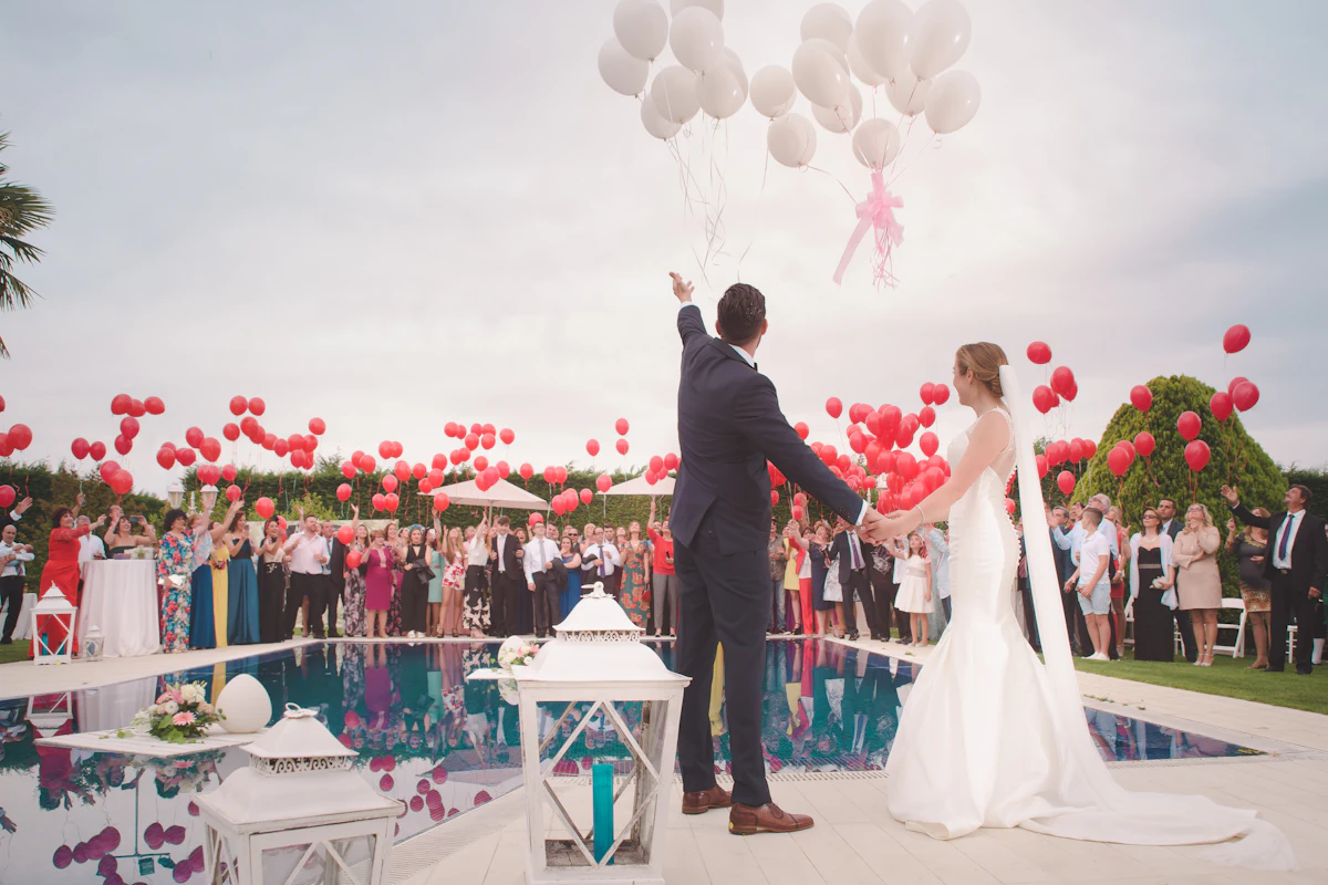 Couple holding hands by a pool as red balloons float into the sky
