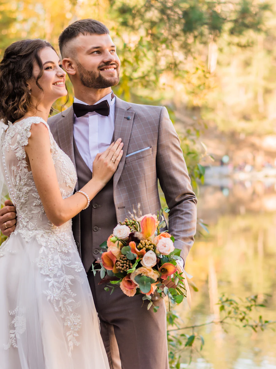 Sarah and James smiling by a lake in autumn, bouquet in hand