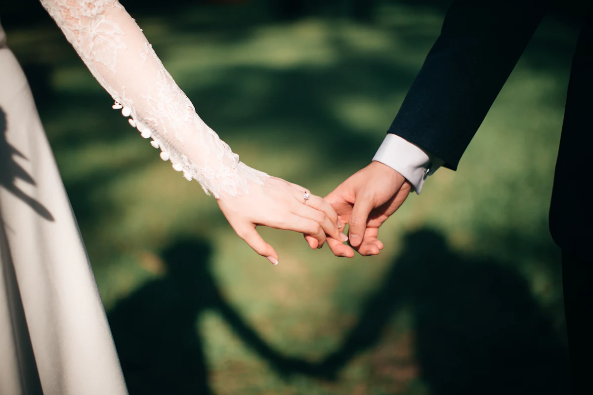 Close-up of a couple holding hands, their shadows cast on the grass